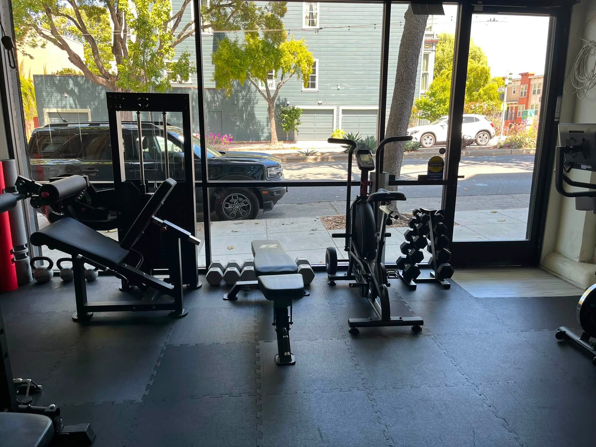 Natural light fills the studio’s training area, with benches, dumbbells and a fan bike.
