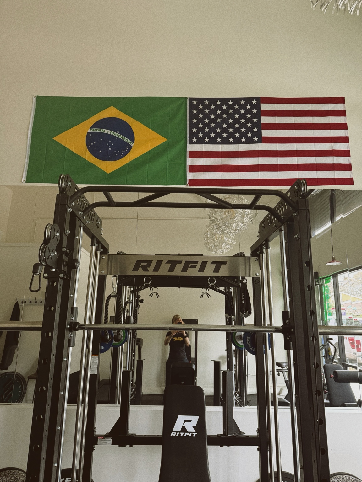 The studio’s Smith machine and cable station beneath Brazilian and American flags.
